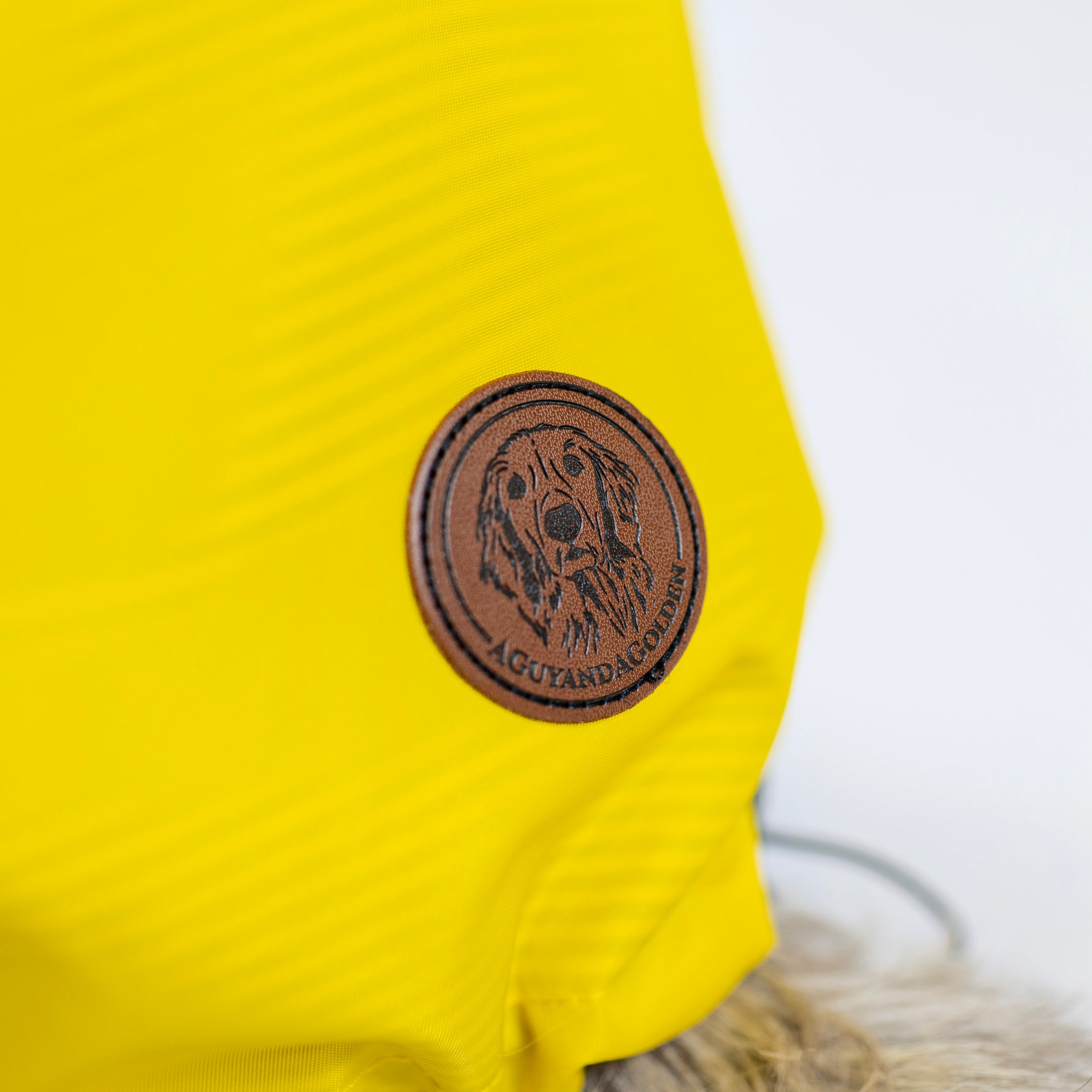 Yellow dog jacket with a brown leather patch featuring a dog logo on a white background
